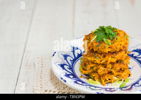 Ein Stapel mit vier süße Kartoffeln und Karotten rostis auf einem blauen und weißen Teller. Stockfoto