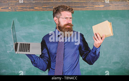 Lehrer bärtigen Hipster hält Buch und Laptop. Mit der rechten Lehre Methode wählen. Lehrer mit modernen pädagogischen Ansatz. Moderne Technologien profitieren. Moderne statt überholt. Digitale gegen Papier. Stockfoto