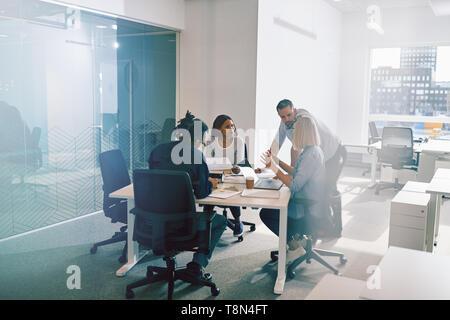 Fokussierter Konzern von verschiedenen Kollegen ein treffen sich gemeinsam um einen Tisch in einem verglasten Büro Stockfoto