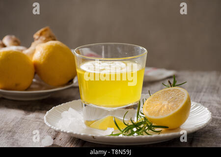 Ingwer Tee mit Zitrone, Ingwer Wurzel und rosemarry auf Holz- Hintergrund. Kleines Glas transparent Krug mit heißen Getränk. Saisonale Getränke. Flache DOF Stockfoto