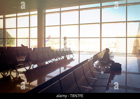 Glasfenster der Abflughalle im Flughafen mit einem Mädchen sitzen auf Stühlen warten auf Ihren Flug Stockfoto