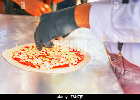 Pizzabäcker vorbereiten, indem Sie eine Pizza Zutaten auf den Teig mit Tomatensoße und Mozzarella. Italienische Küche. Berühmte Rezept. Leckeres Essen Stockfoto