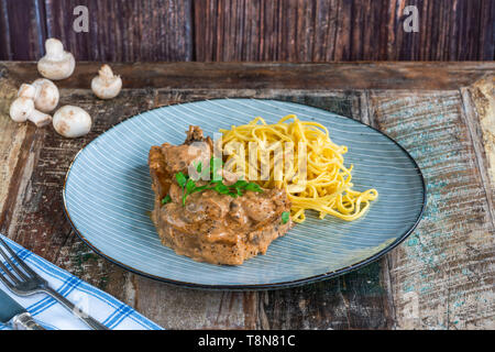 Schweinekoteletts in Cremigen cajun Sauce mit Champignons und Eiernudeln, garniert mit Petersilie. Stockfoto