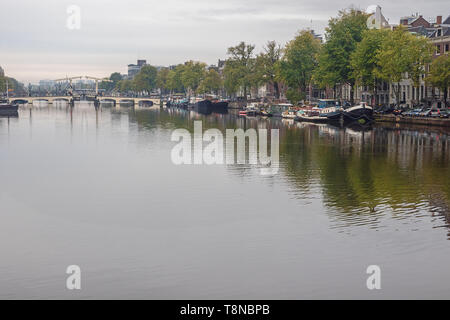 Das dünne Brücke überspannt den Fluss mit Booten an beiden Ufern des Flusses Amstel Stockfoto