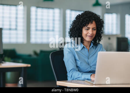 Lächelnd geschäftsfrau an ihrem Schreibtisch arbeiten auf einem Laptop Stockfoto
