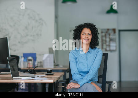 Lächelnden jungen Geschäftsfrau an ihrem Schreibtisch sitzen in einem Büro Stockfoto