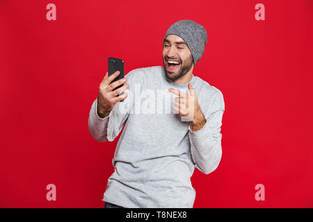 Bild der europäischen Mann 30 s mit Bart und Schnurrbart holding Smartphone beim Stehen über den roten Hintergrund isoliert Stockfoto