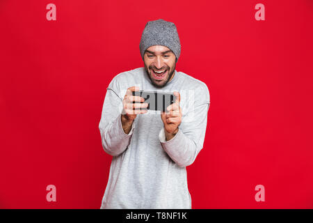 Bild von fröhlichen Menschen 30 s Smartphone halten und Spielen von Videospielen über den roten Hintergrund isoliert Stockfoto