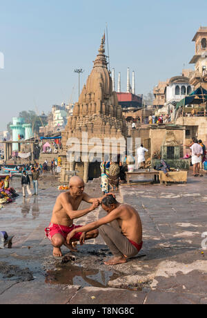 Der Mensch erhält seinen Kopf vor der schiefen Ratneshwar Mahadev Tempel durch den Ganges, Varanasi, Indien rasiert Stockfoto