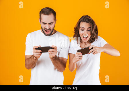 Bild von freudiger Mann und Frau gemeinsam Videospiele auf Smartphones über Gelb Hintergrund isoliert Stockfoto