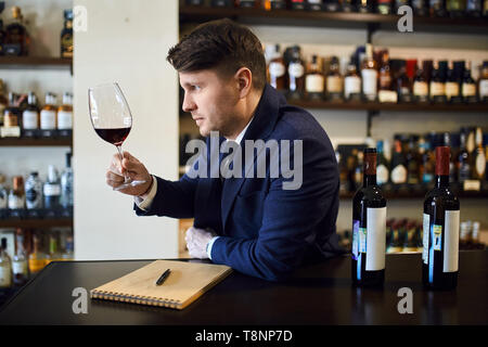 Nette junge Mann in modischen blauen Anzug am Tisch sitzen und Verkostung der trinken. Bis schließen Seitenansicht Foto. Stockfoto
