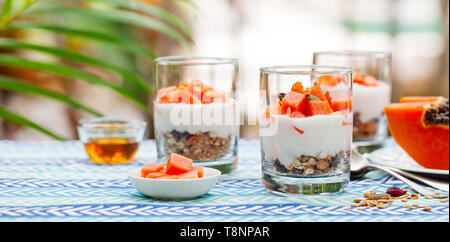 Dessert mit Papaya, Joghurt und Müsli in Gläsern. Im Hintergrund. Stockfoto