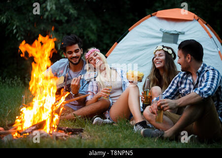 Gruppe von Freunden campen. Sie sitzen um Lagerfeuer, Gitarre spielen Stockfoto