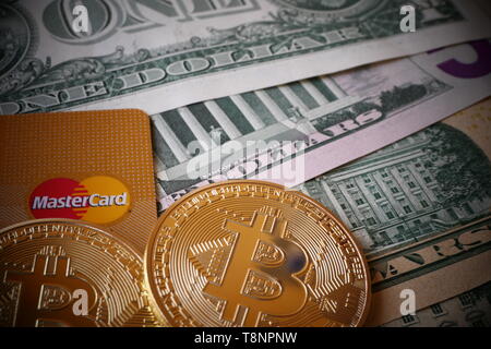 BERLIN, DEUTSCHLAND - Dezember 1, 2018: Bitcoins, eine virtuelle Währung in körperlicher Form, auf US-Dollar Noten und eine MasterCard Kreditkarte Stockfoto