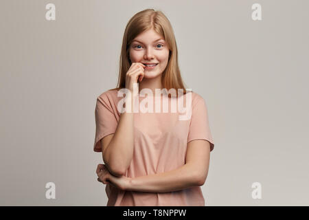 Nervös emotionale schönes Mädchen in beige T-Shirt fühlt sich ängstlich und überrascht, beißt Nägel in Verwirrung sorgen vor Prüfungen. close up Portrait. Isolierte grauen Hintergrund. emotion Konzept Stockfoto