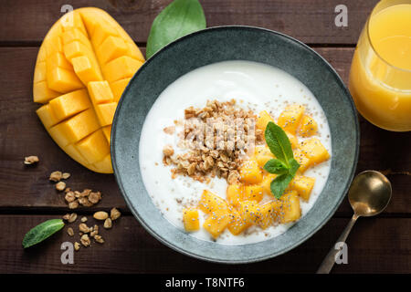 Frühstück Joghurt Schale mit Mango und Müsli auf einem Holztisch, Hintergrund, Ansicht von oben Stockfoto