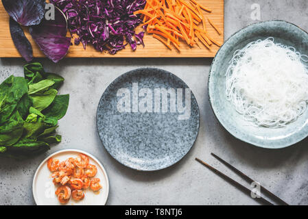 Gesundes Essen Vorbereitung Hintergrund. Asiatische Küche essen. Rotkohl, Gurken, Glas Reis Nudeln, Spinat und Krabben. Ansicht von oben. Grauer Beton backd Stockfoto