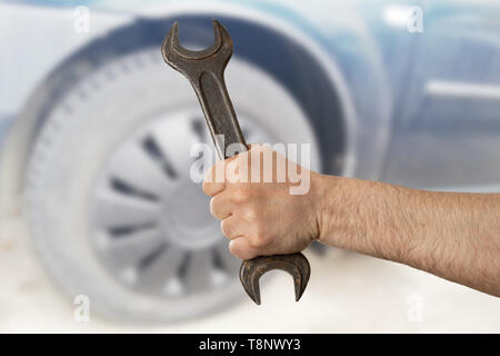 Männliche Mechaniker holding Stahl Schraubenschlüssel konzentriert closeup mit Autoreifen im Hintergrund Stockfoto