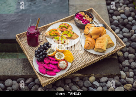 Frühstück auf einem Tablett mit Obst, Brötchen, Avocado Sandwiches, smoothie Schüssel am Pool. Sommer gesunde Ernährung, Veganes Frühstück. Lecker Ferienhäuser Konzept Stockfoto