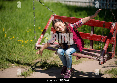 Lächelnd kleine Mädchen mit langen Zöpfen ist auf der Schaukel im Park. Stockfoto