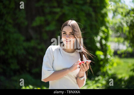 Lächelnde Junge brünette Frau hält Ihr Telefon im Park. Stockfoto