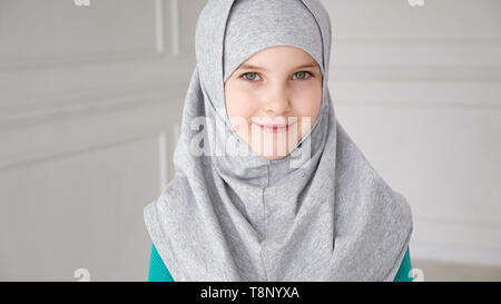 Portrait von muslimischen 9-Jahre alt jugendlich Mädchen in Grau hijab Sucht in Kamera und Lachen. Stockfoto