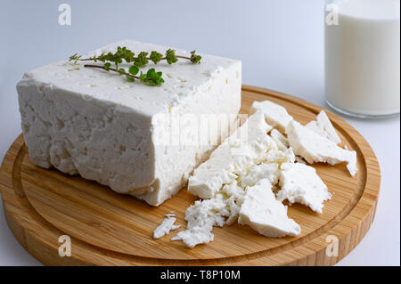 Großes Stück traditioneller griechischer Schafskäse auf Holz Schneidebrett mit Oregano und eine Flasche Milch auf weißem Hintergrund Stockfoto