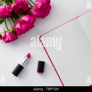 Rosa Lippenstift und Rosen Blumenstrauß mit leeren Notepad auf weißem Hintergrund. Stockfoto
