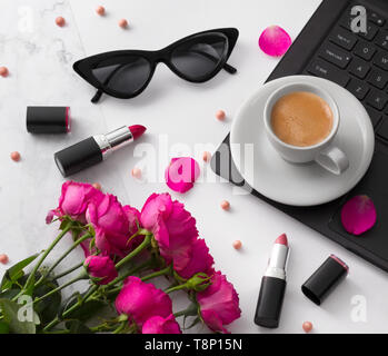 Blumenstrauß aus Rosen, Tasse Kaffee, Laptop, Sonnenbrille und Lippenstift auf weißer Tisch. Stockfoto