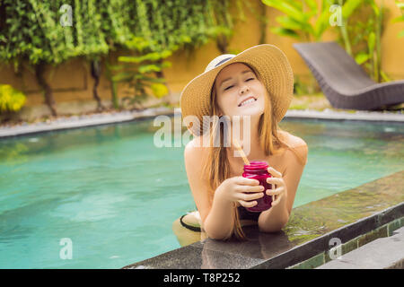 Junge Frau trinkt Dragon Fruit Smoothies auf dem Hintergrund der Pool. Fruit Smoothie - gesunde ernährung Konzept. Nahaufnahme von detox Smoothie mit Stockfoto