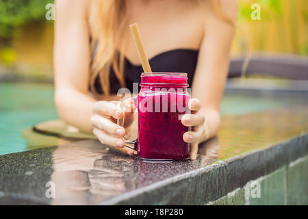 Junge Frau trinkt Dragon Fruit Smoothies auf dem Hintergrund der Pool. Fruit Smoothie - gesunde ernährung Konzept. Nahaufnahme von detox Smoothie mit Stockfoto