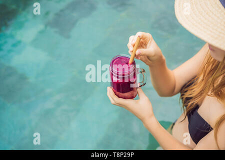 Junge Frau trinkt Dragon Fruit Smoothies auf dem Hintergrund der Pool. Fruit Smoothie - gesunde ernährung Konzept. Nahaufnahme von detox Smoothie mit Stockfoto