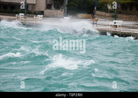 Stürmische See plätschern die Wellen an der Küste Promenade mit Bänken in Dalmatien Stadt am Meer in der Nebensaison bei starkem Südwind mit Regen Stockfoto