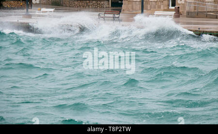 Stürmische See plätschern die Wellen an der Küste Promenade mit Bänken in Dalmatien Stadt am Meer in der Nebensaison bei starkem Südwind mit Regen Stockfoto