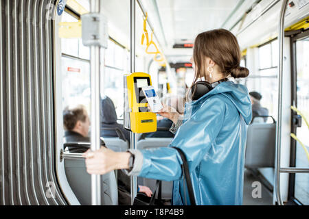 Frau Zahlung conctactless mit Smartphone für die öffentlichen Verkehrsmittel in der Straßenbahn Stockfoto