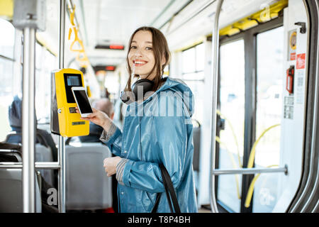 Portarit eines junge lächelnde Frau Zahlung conctactless mit Smartphone für die öffentlichen Verkehrsmittel in der Straßenbahn Stockfoto