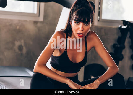 Junge kaukasier schöne weibliche fitness Modell auf Schweiß Sportkleidung tragen und sitzen auf Laufband im Fitnessstudio. Gesundheit und Sport portrait Konzept Stockfoto
