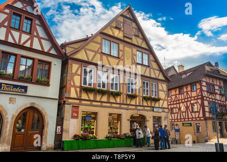 Malerische Aussicht auf eine Reihe von bunten Fachwerkhäusern und Geschäften mit Menschen vor auf einer Straße mit Kopfsteinpflaster in der mittelalterlichen Stadt Rothenburg ob... Stockfoto