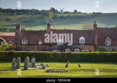 Zeitraum Cottages in Turville gesehen über den Kirchhof mit Cobstone Windmühle auf dem Hügel über. Stockfoto