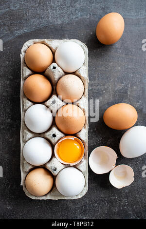 Frische organische rohe Eier, weiss, beige und braun, einer ist gerissen Stockfoto