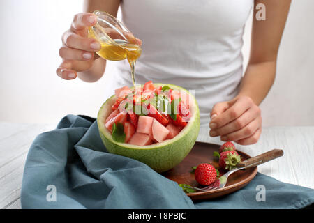 Frau gießen Honig auf köstliche Frucht Salat in der Melone Schüssel Stockfoto