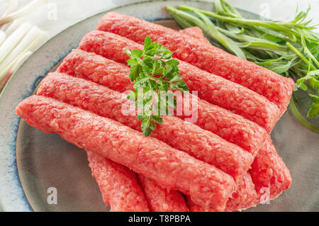 Chevapchichi ist eine nationale Balkan Teller. Nahaufnahme einer Reihe von frischem rohem Rindfleisch Döner auf einem Teller. Stockfoto