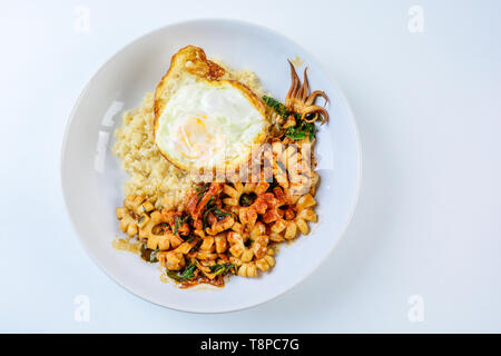 Würzig gebratener Tintenfisch mit Basilikum und Chili rühren, sunny side up Ei, serviert mit braunem Reis. Heiß und würzig Gericht. Stockfoto