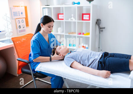 Friedliche qualifizierte asiatische Frau massieren Kopf und Hals der Lüge boy Stockfoto