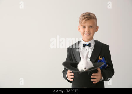 Süße kleine Magier holding Hut mit Kaninchen auf hellen Hintergrund Stockfoto