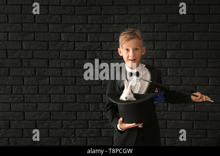 Süße kleine Magier holding Hut mit Kaninchen gegen dunkle Mauer Stockfoto