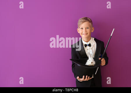 Süße kleine Magier holding Hut mit Kaninchen auf farbigen Hintergrund Stockfoto