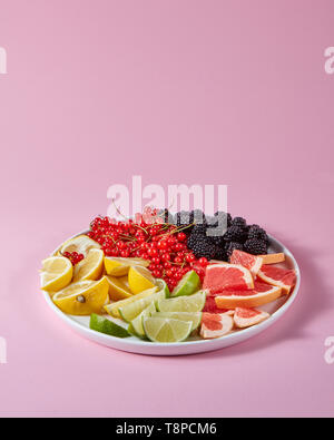 Satz von verschiedenen Zitrusfrüchten und Beeren in eine Platte auf einem rosa Hintergrund mit Kopie Raum vorgestellt. Gesunde Vitamin Essen Stockfoto