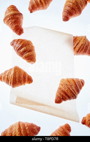 Floating frisch gebackenen Croissant auf einem hellen Hintergrund Pergamentpapier, Mock up. Stockfoto