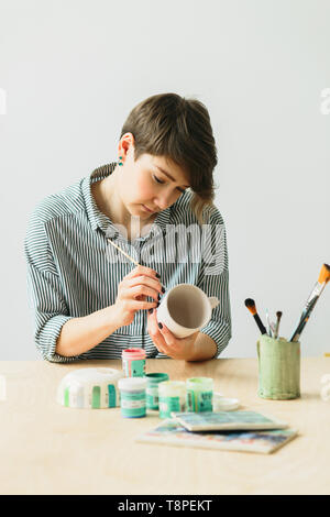 Die Töpferei Frau hält in der Hand einen Becher das Ornament zu malen, handgefertigte Keramik Stockfoto